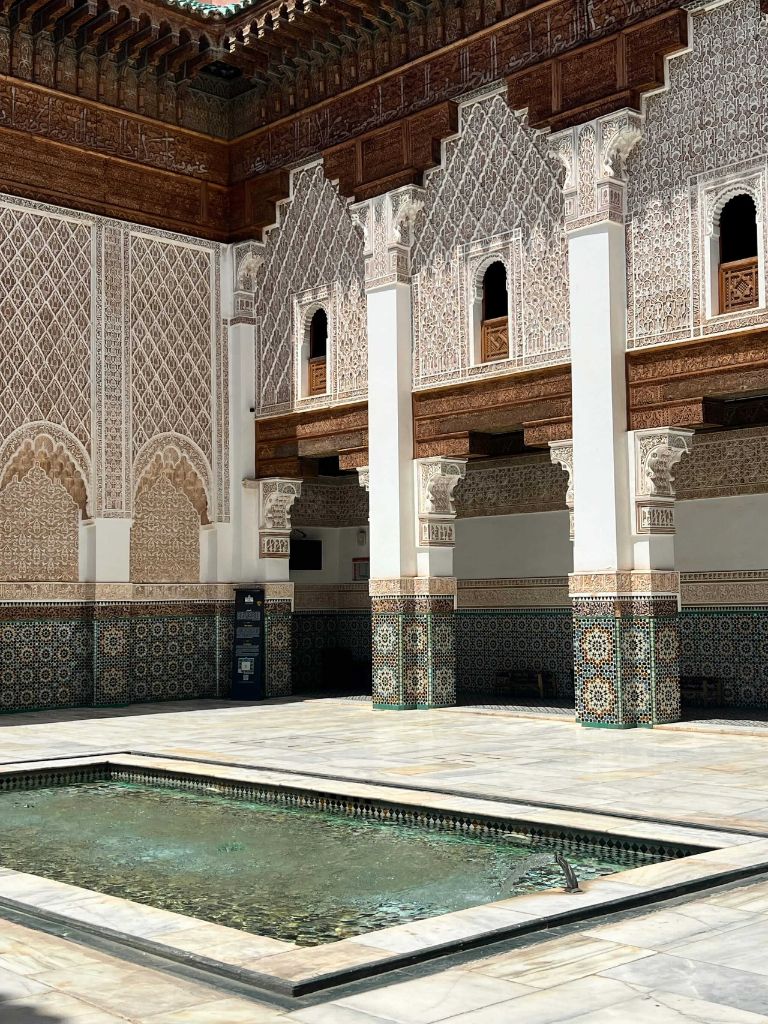 Cour intérieure d'une medersa de Marrakech avec stucs sculptés, carrelage zellige et bassin central en marbre