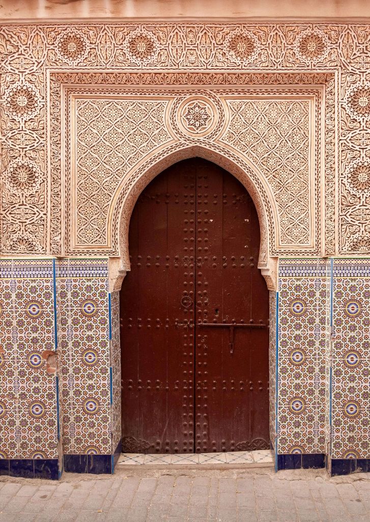 Porte traditionnelle marocaine en bois sculpté sous une arche en zellige multicolore dans la Médina de Marrakech